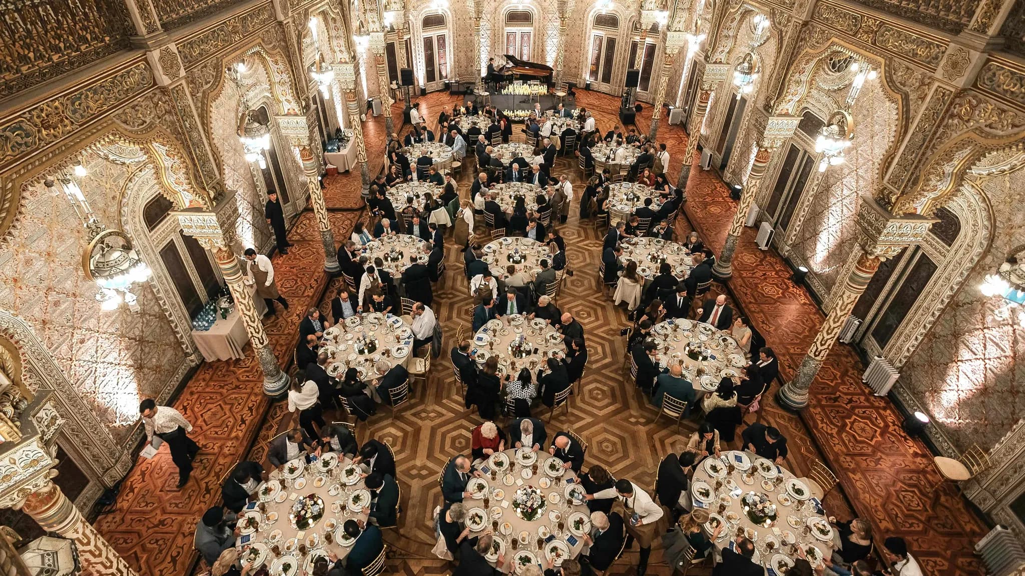 Gala dinner in an ornate Moorish-style hall, with guests seated at round tables beneath chandeliers